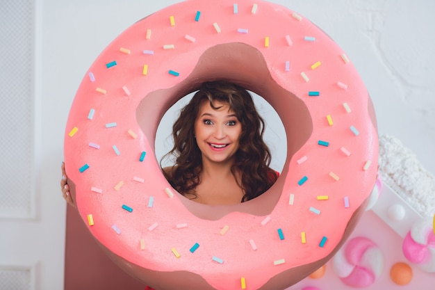 Leuk meisje poseren met roze donuts, gek rond, dessert, slecht eten, kijkt in het gat in de donut, houdt donuts bij de ogen