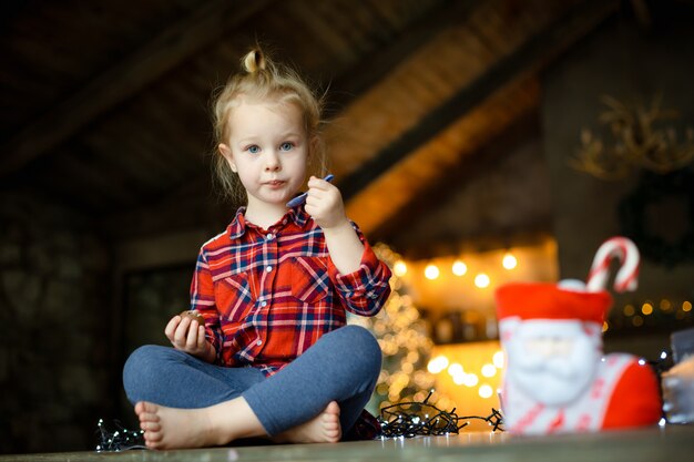 Leuk peutermeisje die de zitting van het chocoladeei in een jachthuis eten dat voor Kerstmis wordt verfraaid.