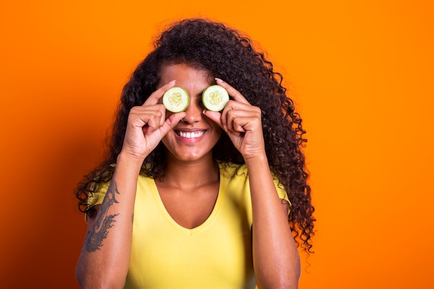 Leuk portret van mooi zwart afrikaans model met een plakje komkommer tegen haar oog, verjongend huidverzorging regime behandeling gezichtsschoonheid concept.