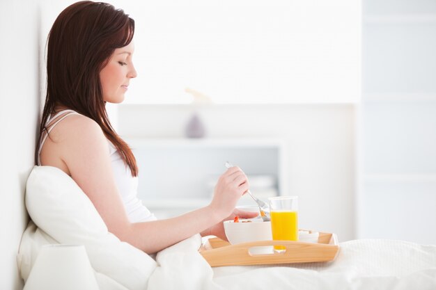 Leuk roodharig wijfje dat een glas jus d&#39;orange drinkt terwijl het zitten op haar bed