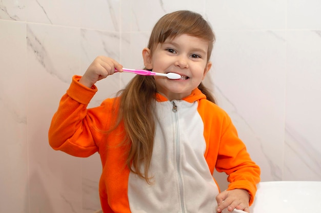 Leuk schattig babymeisje dat een tandenborstel vasthoudt en haar tanden poetst in de badkamer. Kind leert gezond te blijven. Ochtend gezonde hygiëne voor kinderen.