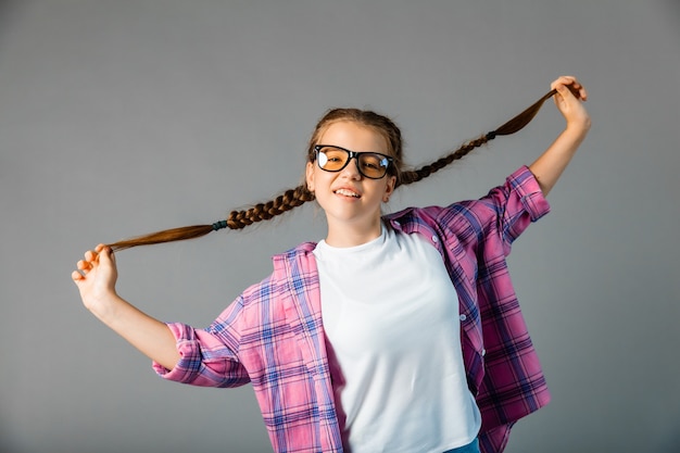 ... Leuk schoolmeisje. Meisje met gevlochten haar. grijze achtergrond. Klein meisje speelt met staartjes.