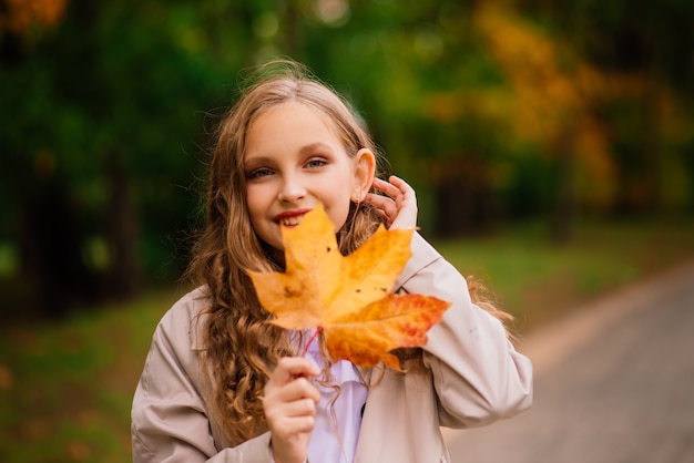 Leuk stijlvol meisje met lang blond haar in het herfstpark. Herfst kindermode, lifestyle portret.