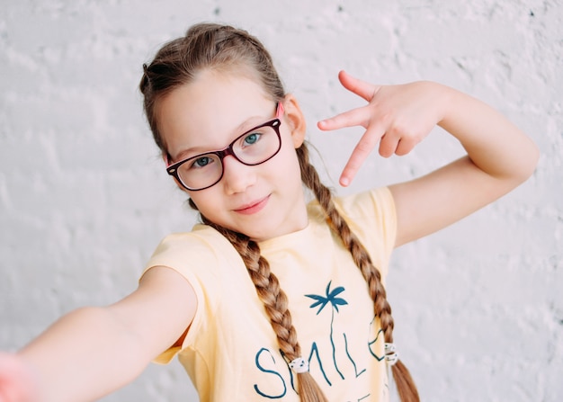 Leuk tweensmeisje in gele t-shirt met grappige vlechten die selfie op frontale camera nemen