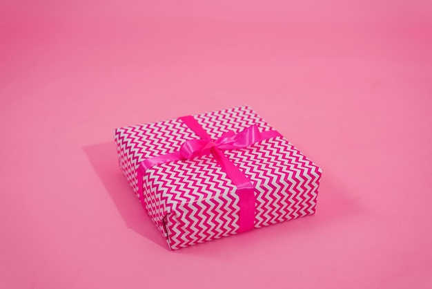 Leuk verrassingscadeau verpakt in stijlvol roze en wit papier met fuchsia strik op roze achtergrond met kopieerruimte