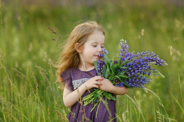 Leuk, vierjarig meisje in violette kleding houdt boeket van lupinebloemen in handen