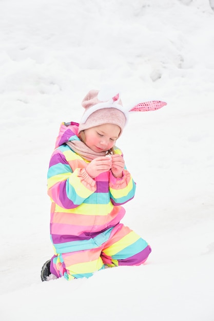 Leuk vrolijk kleutermeisje met caranale konijnenoren die in de sneeuw sneeuw spelen in de winterpret van de paashaas in april