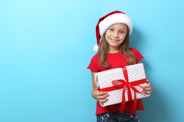 Leuk vrolijk meisje in een kerstmuts op een gekleurde achtergrond met een cadeau