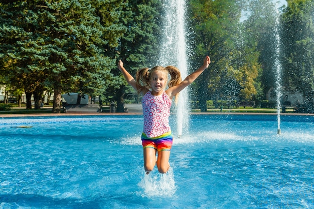 Leuk vrolijk meisje speelt in de fontein. Het kind heeft plezier in een zomerpark in de stadsfontein.