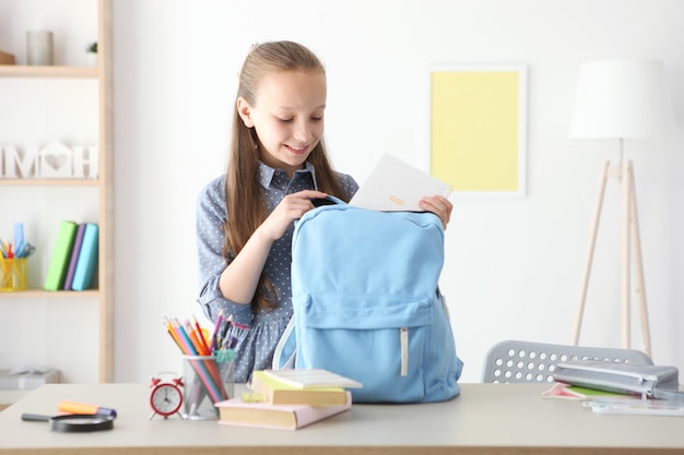 Leuk vrolijk schoolmeisje stopt briefpapier in een rugzak