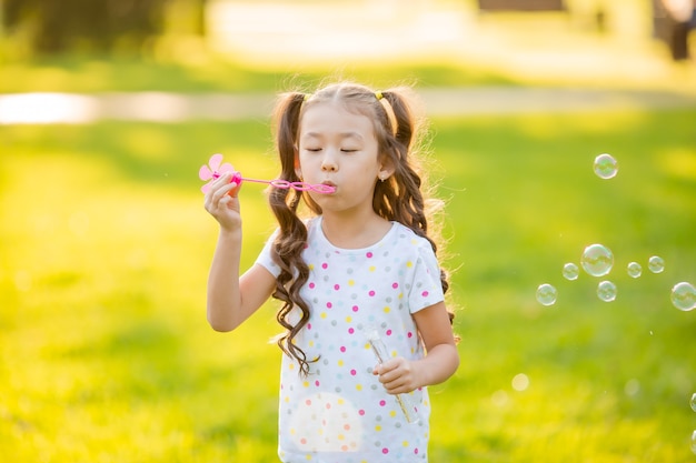 Leuk weinig Aziatisch meisje in de zomer op een wandeling die zeepbellen blaast