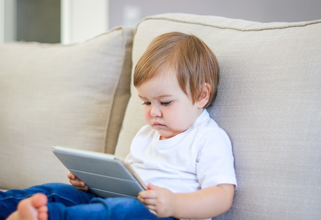 Leuk weinig baby het letten op beeldverhaal op digitale tabletzitting op de bank.