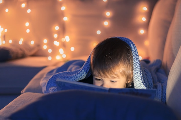 Foto leuk weinig babyjongen die een boek leest dat op bank ligt