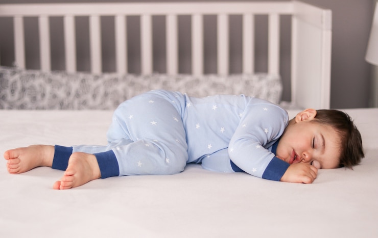 Foto leuk weinig babyjongen in het lichtblauwe pyjama's slapen vreedzaam thuis op bed.