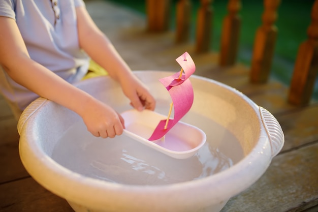 Leuk weinig jongen die met eigengemaakt schip in bassin water op de portiek van huis speelt. kinderen spelen.