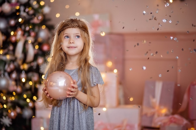 Leuk weinig lachend blondemeisje met lang haar dat een bal van Kerstmis houdt