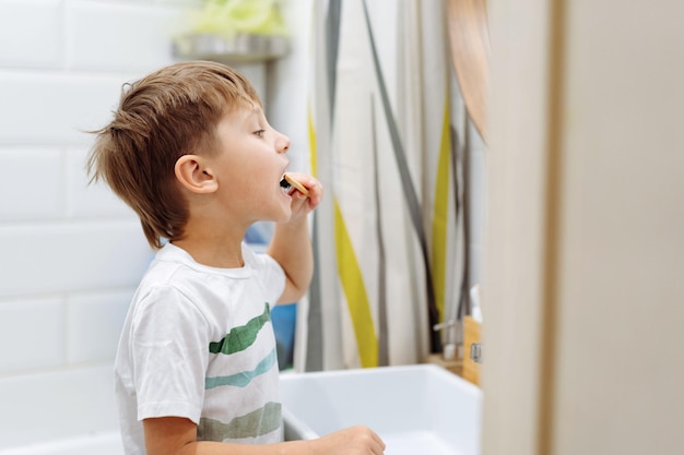 Leuke 5-jarige jongen tandenpoetsen met bamboe tandenborstel in badkamer Afbeelding met selectieve focus