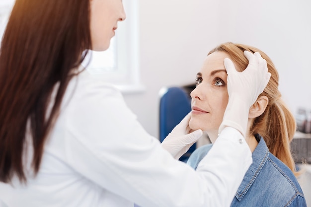 Leuke aangename aantrekkelijke vrouw zitten en kijken naar haar dokter terwijl ze in het dokterskantoor is