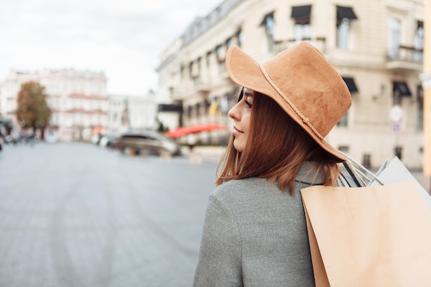 Leuke aantrekkelijke shopaholic grappige vrouw in herfstjas en hoed met veel papieren boodschappentassen in de Europese stad