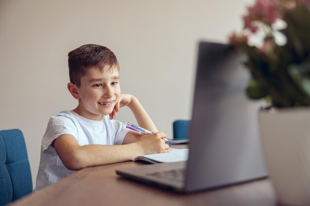 Leuke aardige kleine jongen leerling luistert naar leraar tijdens online videoles thuisonderwijs