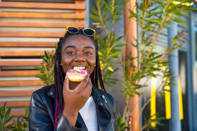 Leuke Afrikaanse vrouw die een kleurrijke donut eet.