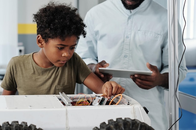 Leuke afro-amerikaanse schooljongen aansluitkabels van speelgoedrobot