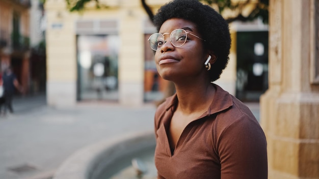 Leuke Afro-Amerikaanse vrouw met een bril die op straat zit te luisteren