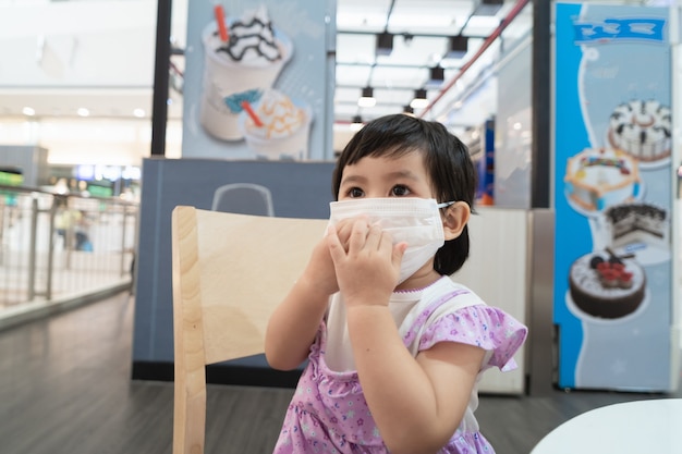 Leuke Aziatische baby die chirurgisch masker draagt en op het stoel wachtende roomijs in het restaurant zit