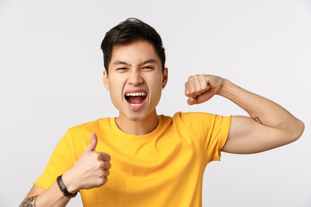 Leuke Aziatische mens in gele t-shirt die spier en duim tonen