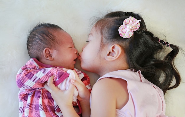 Leuke Aziatische zuster die pasgeboren baby kussen die op witte bontachtergrond ligt.
