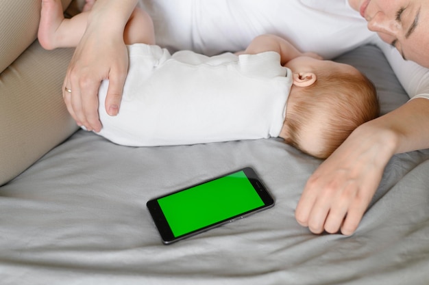 Foto leuke baby en moeder knuffelen thuis in bed naast de telefoon kleur sleutel kind veiligheid en bescherming