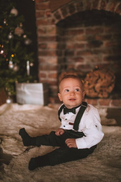 Foto leuke baby jongen zit op de vloer tegen de kerstboom thuis