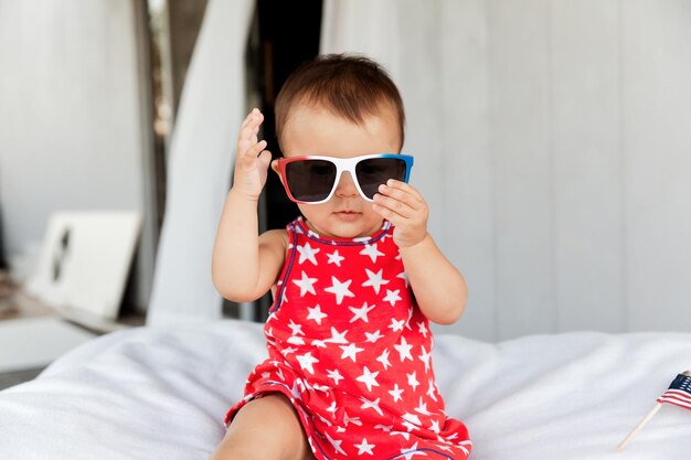 Leuke baby met een zonnebril terwijl ze thuis op bed zit.