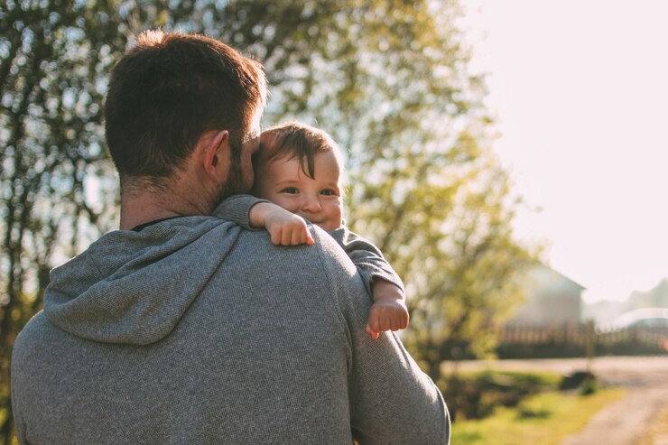 Leuke babyjongen die op zijn papaschouders op de dorpsweg in openlucht lopen