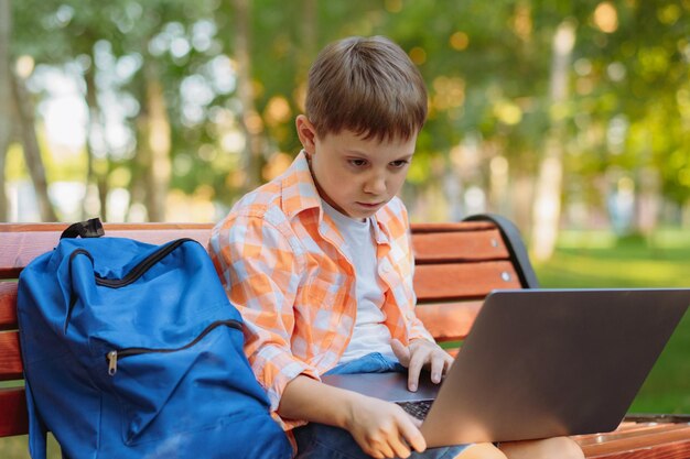 Leuke blanke jongen die op een bankje in het park zit met een zwart scherm op een laptop