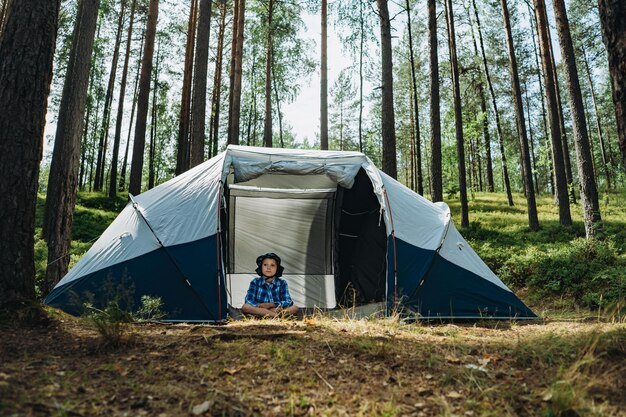 Leuke blanke jongen met een hoed die in een groot toeristisch tentfamiliekampeerconcept zit