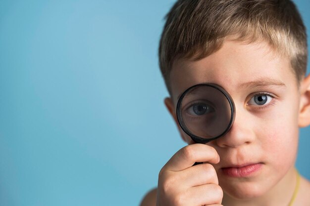 Leuke blanke jongen met een vergrootglas naar het oog grappige jongen die door vergrootglas kijkt