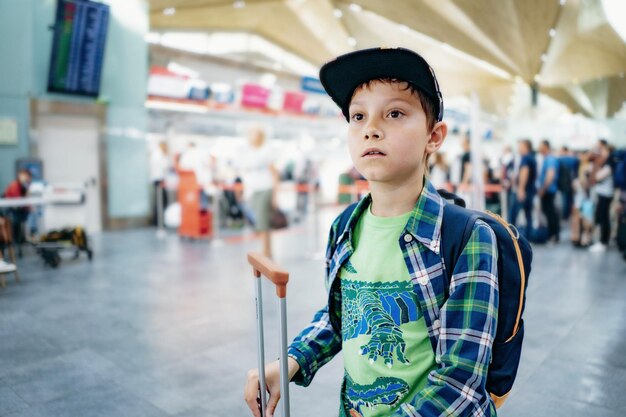 Leuke blanke jongen op de luchthaven met rugzak en koffer reisconcept