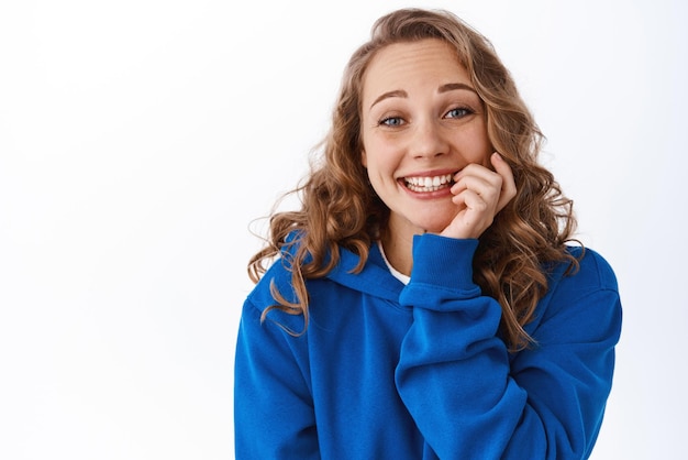 Leuke blanke vrouw met blond krullend haar bijtende vinger en glimlachend verleidde blik met verlangen wil iets opgewonden staren naar camera witte achtergrond