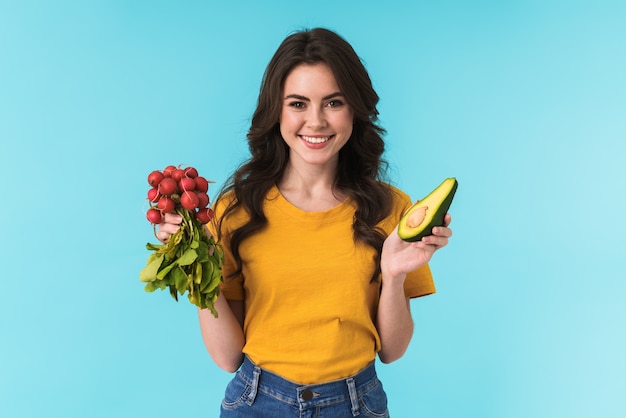 leuke blije gelukkige vrouw poseren geïsoleerd over blauwe muur met avocado en radijs.