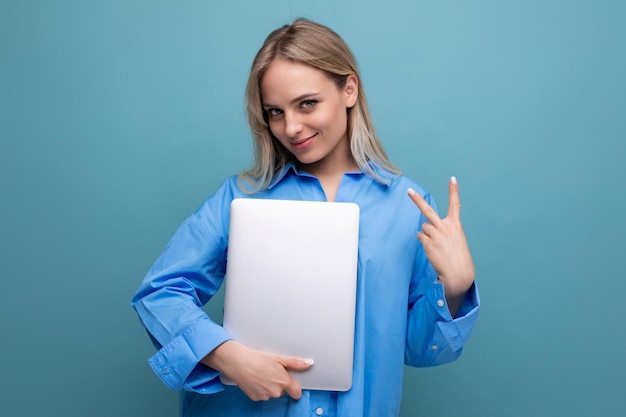 Leuke blonde studente met een laptopcomputer op een heldere blauwe achtergrond