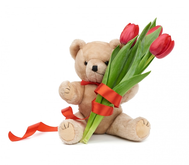 Leuke bruine teddybeer houdt in zijn poot een boeket van rode tulpen