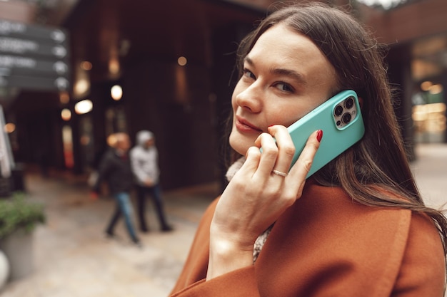 Leuke brunette vrouw in bruine jas praten aan de telefoon in de stad