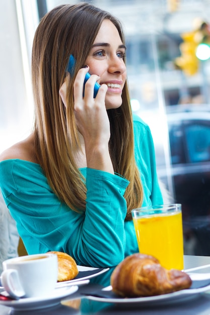 Leuke brunette vrouw in cafe spreekt via mobiele telefoon