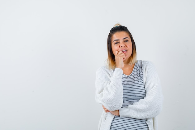 Leuke dame in t-shirt, vest die hand op kin houdt en peinzend kijkt, vooraanzicht.