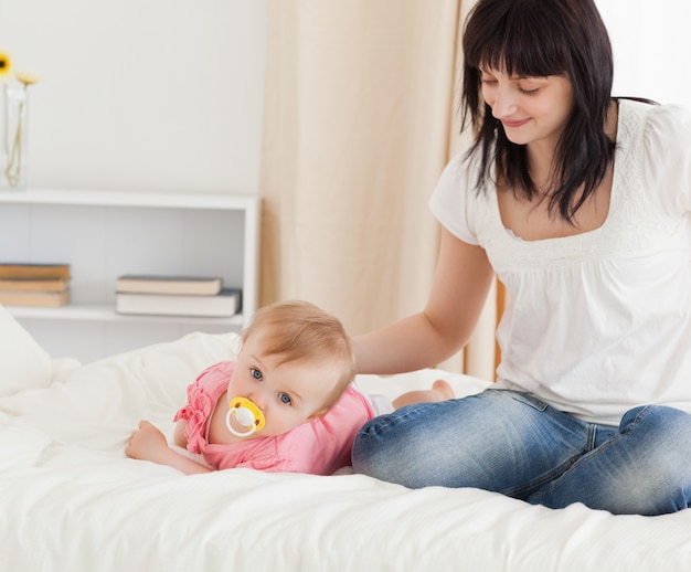 Leuke donkerbruine vrouw die haar het liggen baby op een bed bekijkt