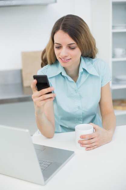 Leuke donkerbruine vrouw die haar smartphone en een kop houdt