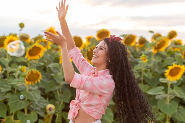 Leuke donkerbruine vrouw die zeepbellen blaast. Mooi veld met zonnebloemen op de achtergrond.