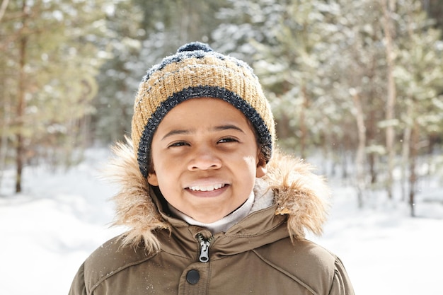 Leuke eigentijdse multi-etnische schooljongen in warme winterkleding die naar de camera kijkt