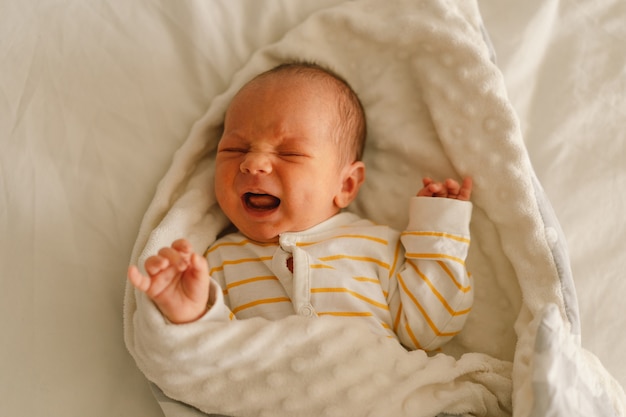 Leuke emotionele pasgeboren kleine babyjongen huilen in de wieg. Buik doet pijn en emotie